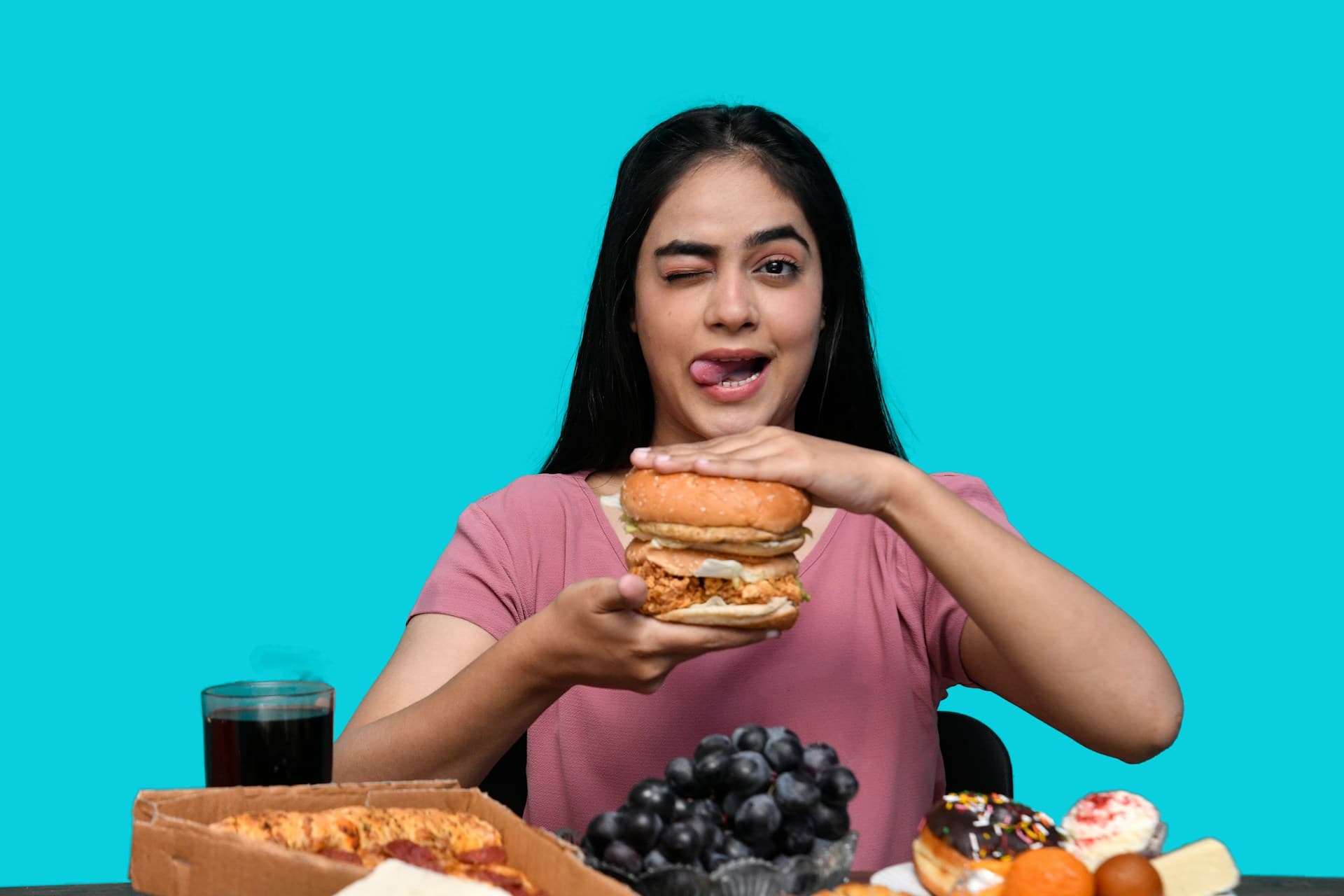 Woman taking a big bite of a burger against a bright turquoise background